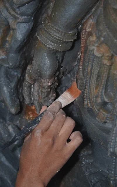 A pair of hands gently cradles a terracotta apsara sculpture, highlighting the intricate carved details and smooth clay texture.