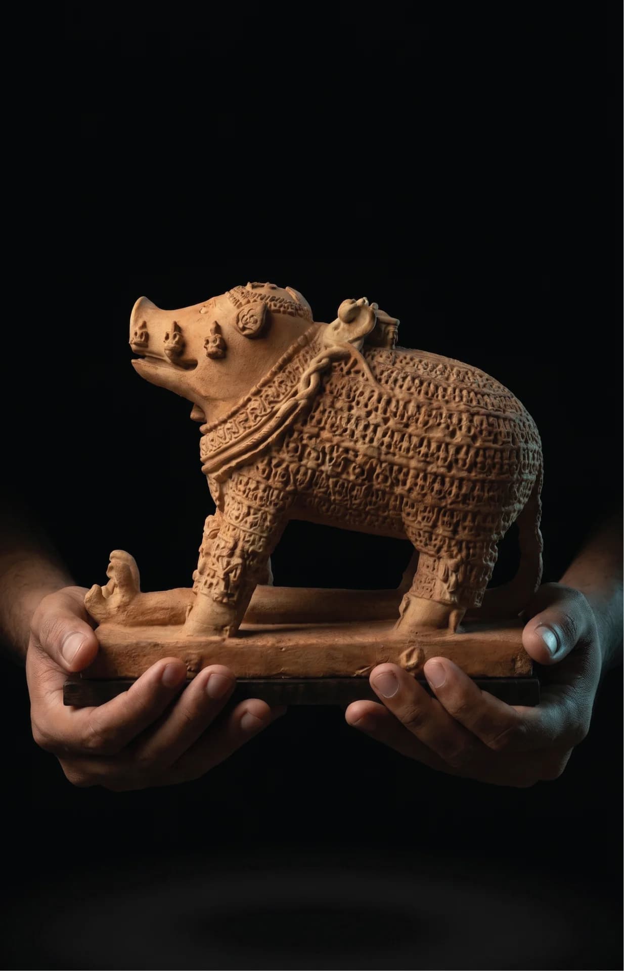 A pair of hands holds a terracotta-style Adi Varaha Sculpture, showcasing the intricate carved details of the boar avatar.