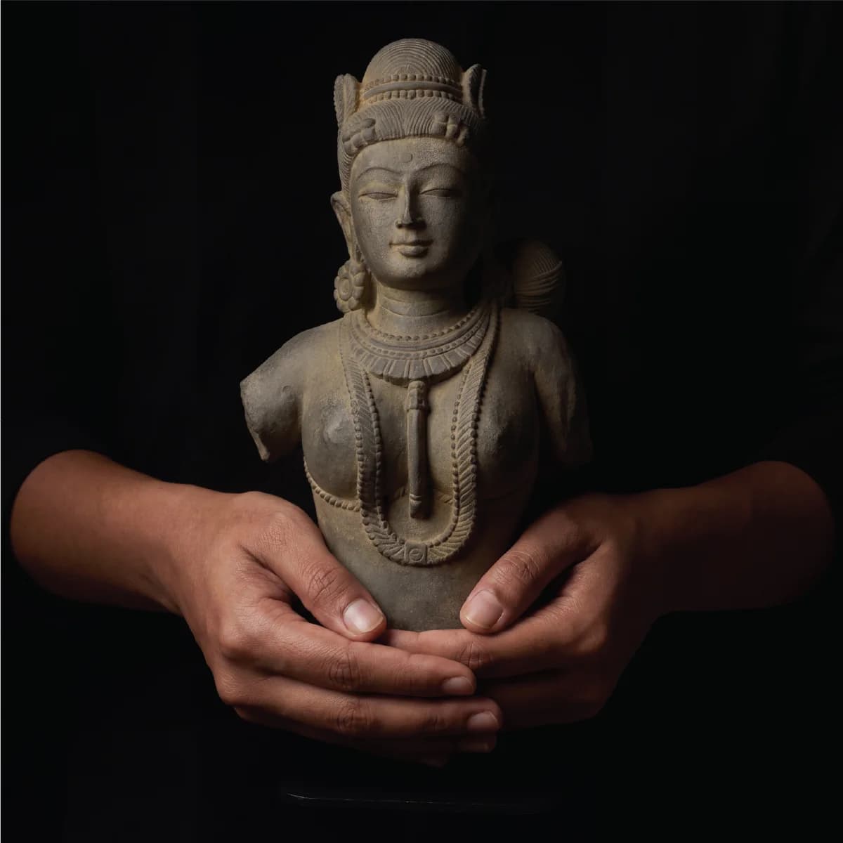 A pair of hands gently cradles a Female Figure Bust Sculpture, showcasing the intricate stone composite Chola-style craftsmanship.