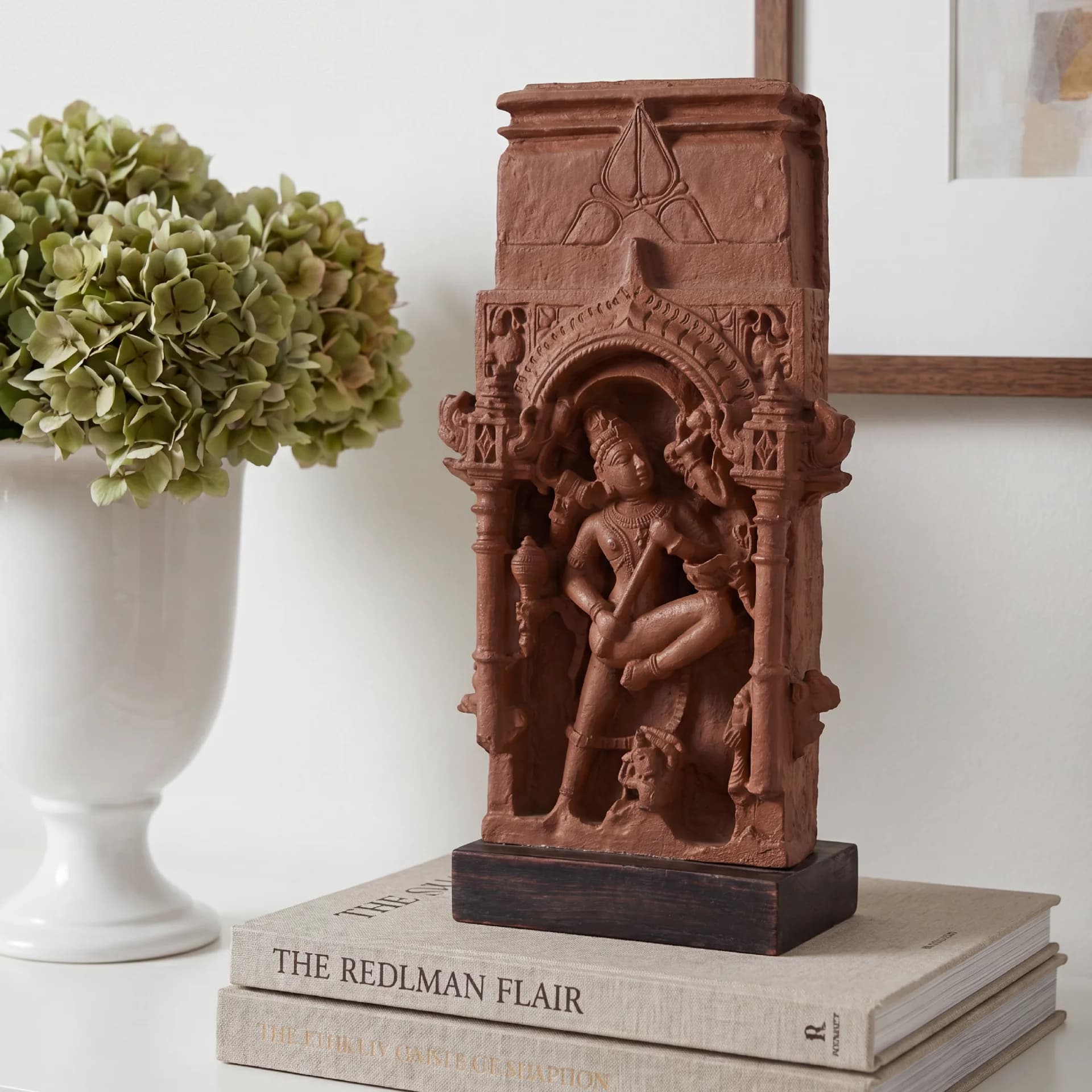 A Gajasura Vadha Sculpture replica in stone composite, displayed on books next to a white vase with green flowers.