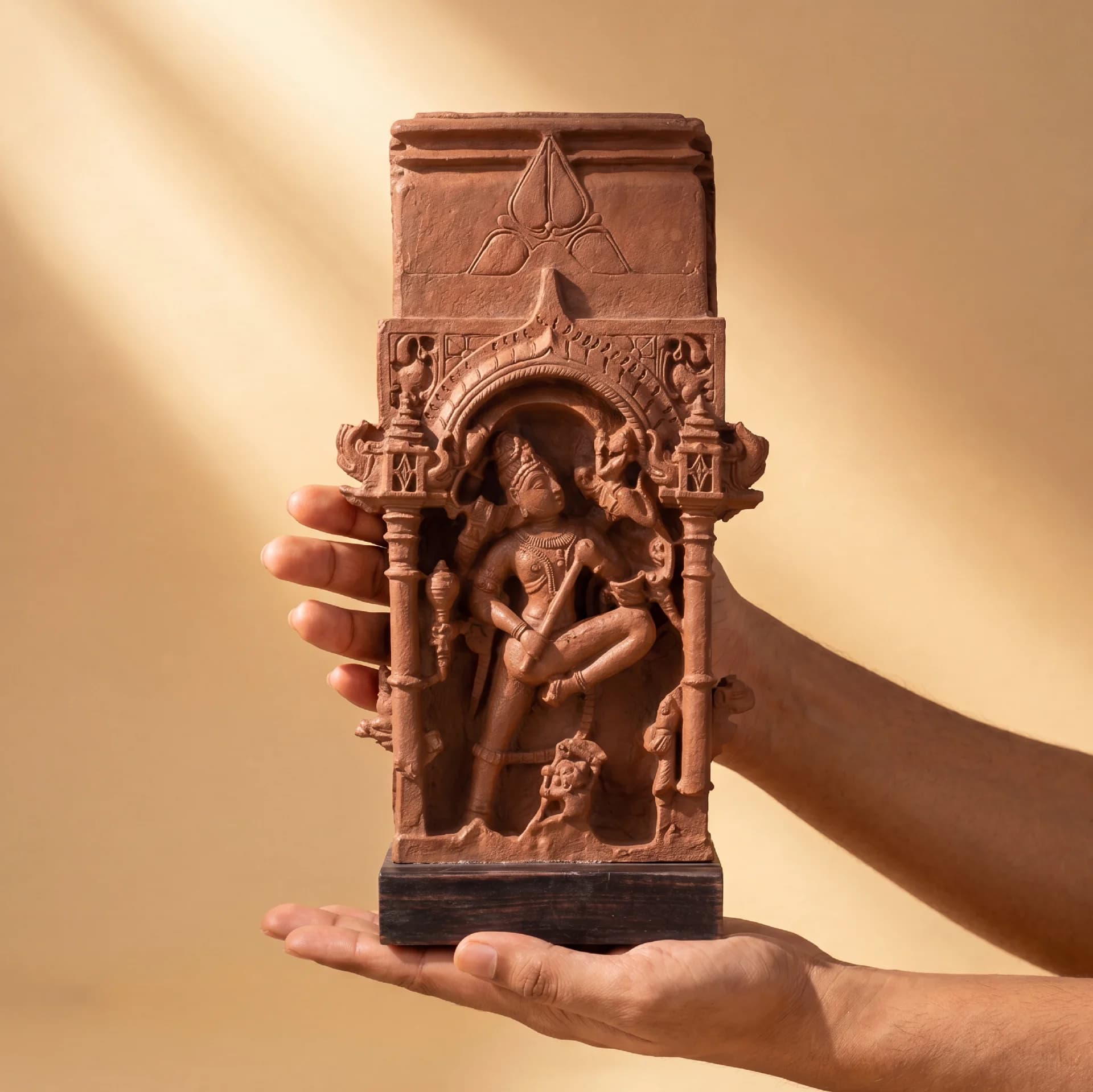 A pair of hands holds the Gajasura Vadha Sculpture, a stone composite replica featuring intricate 10th-century temple relief carvings.