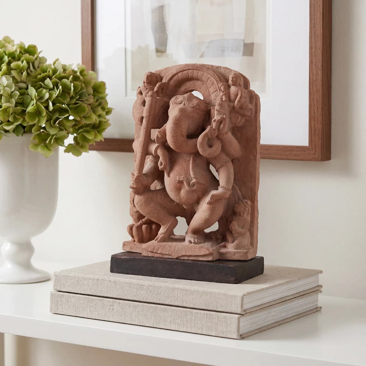 A handcrafted Ganesha Sculpture featuring intricate terracotta-style stone carving, displayed on a stack of books on a white shelf.