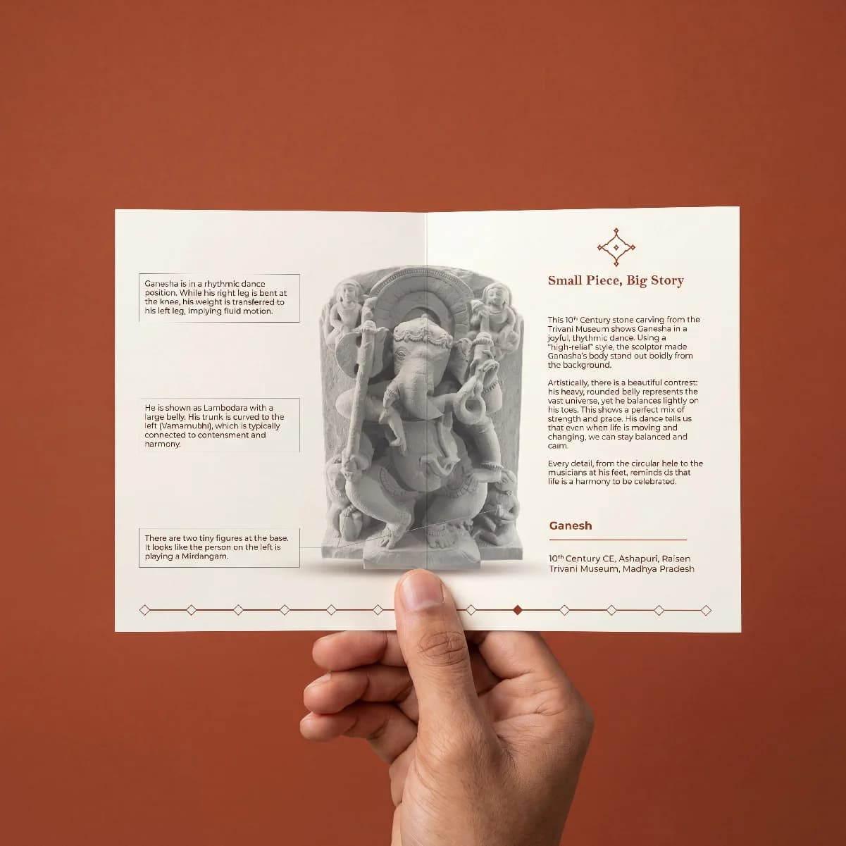 A pair of hands holding an informational brochure about the Ganesha Sculpture, featuring a high-relief stone carving illustration.