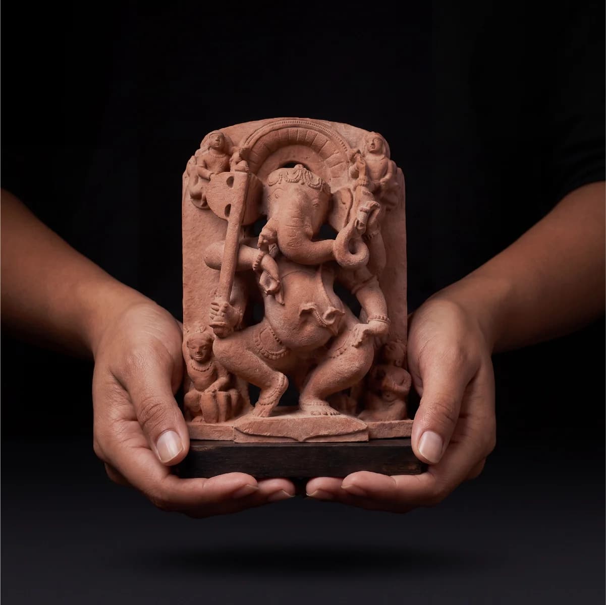 Close-up of two hands holding a terracotta-style Ganesha Sculpture, showcasing the intricate 10th-century temple art details and craftsmanship.