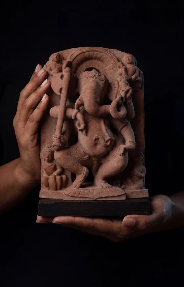 A pair of hands gently cradles the Ganesha Sculpture, a handcrafted terracotta-style replica featuring intricate 10th-century temple art details.