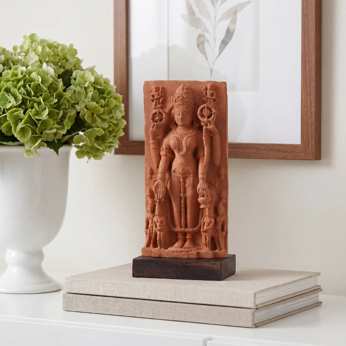 The Gauri Parvati Sculpture, a stone composite replica, stands on stacked books next to a vase of green hydrangeas.