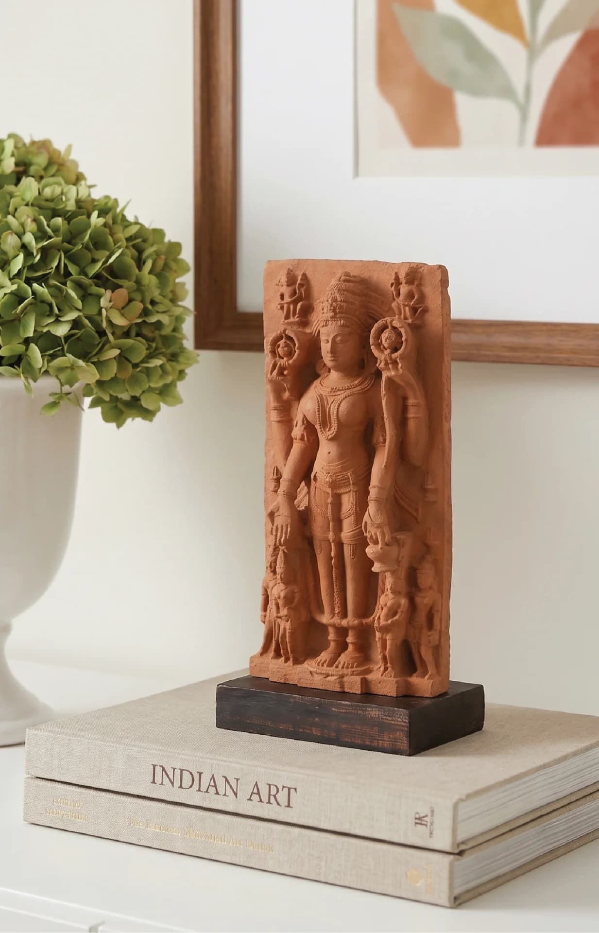 A Gauri Parvati Sculpture replica in stone composite, displayed on a stack of books with a vase nearby.