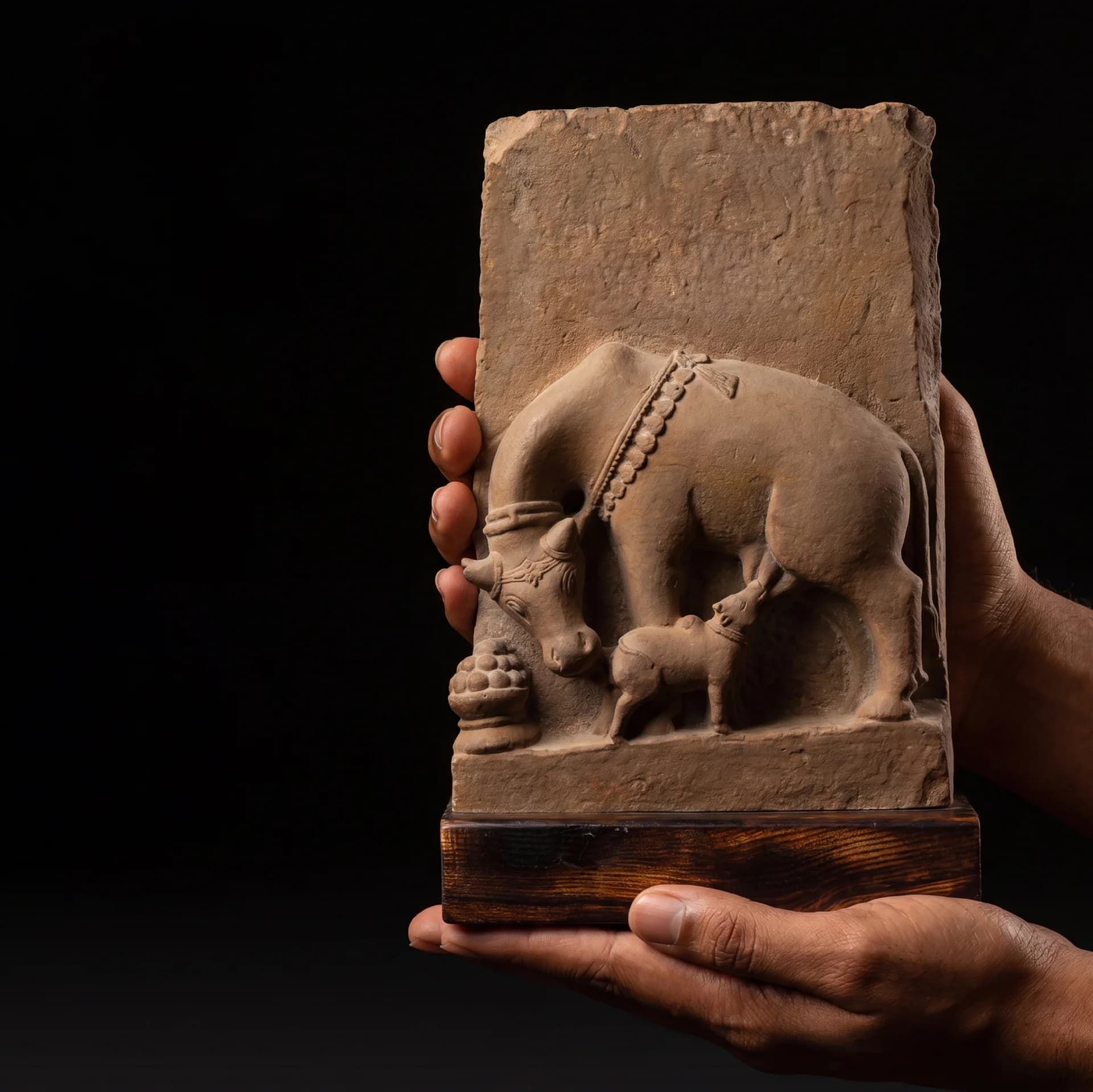 A pair of hands holds a stone composite Kamdhenu Sculpture replica featuring the divine cow nursing her calf.