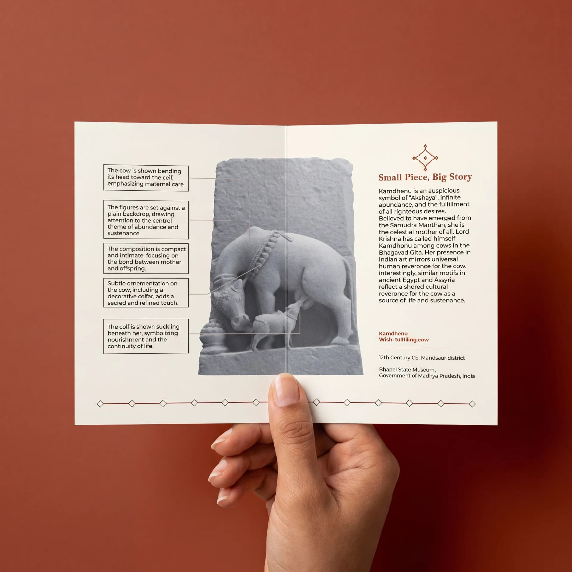 A hand holds an informational brochure featuring the Kamdhenu Sculpture, a stone composite replica of a 12th-century sacred cow artifact.