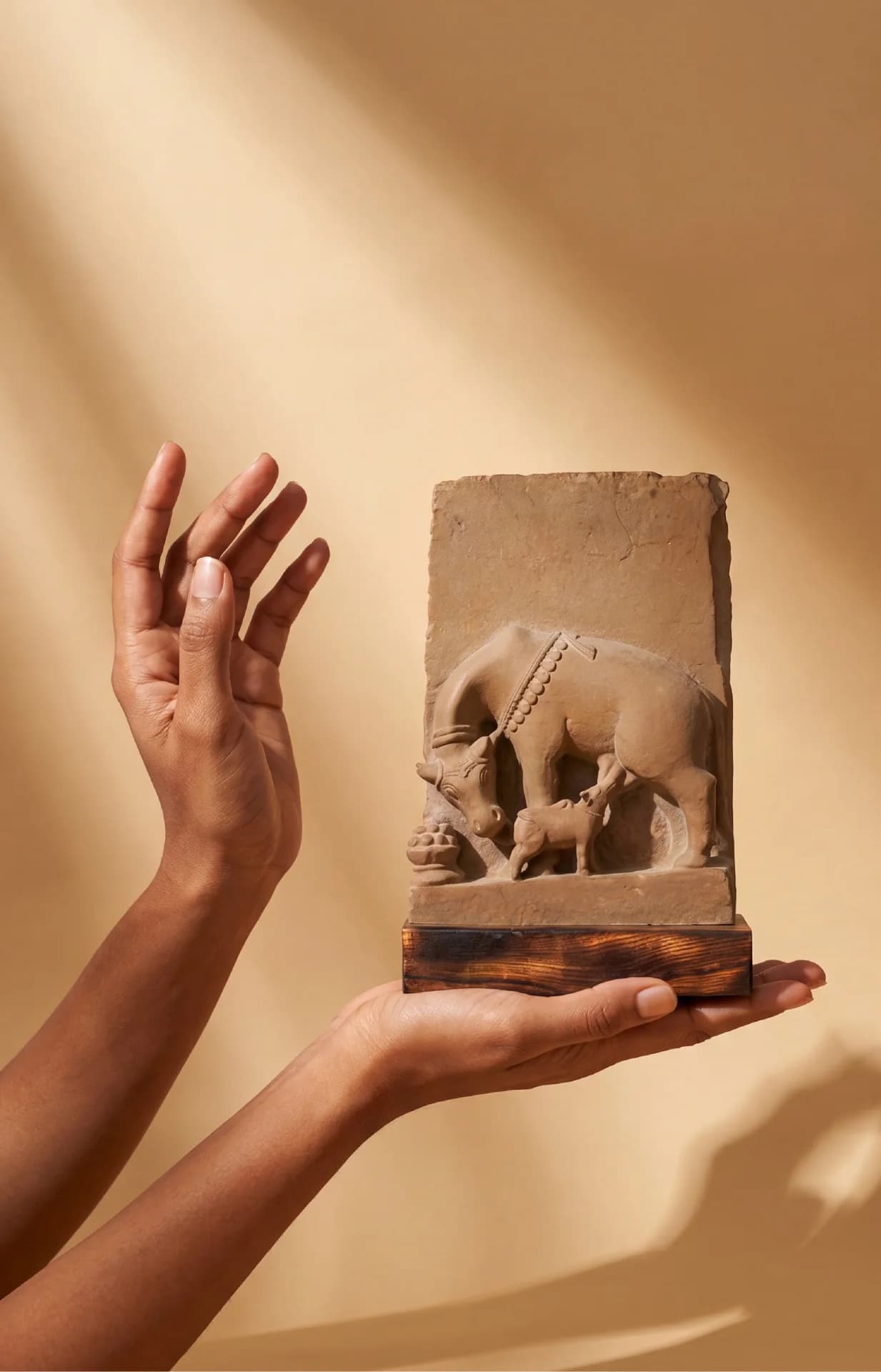 A pair of hands holds a stone composite Kamdhenu Sculpture, showcasing the detailed relief of the cow and calf.