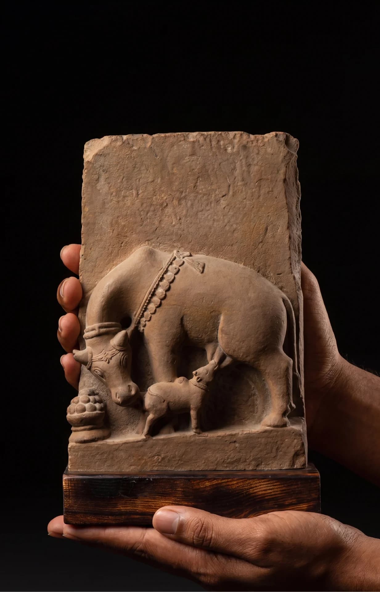 A person holds a hand-finished stone composite Kamdhenu Sculpture, showcasing the detailed relief of the divine cow and calf.