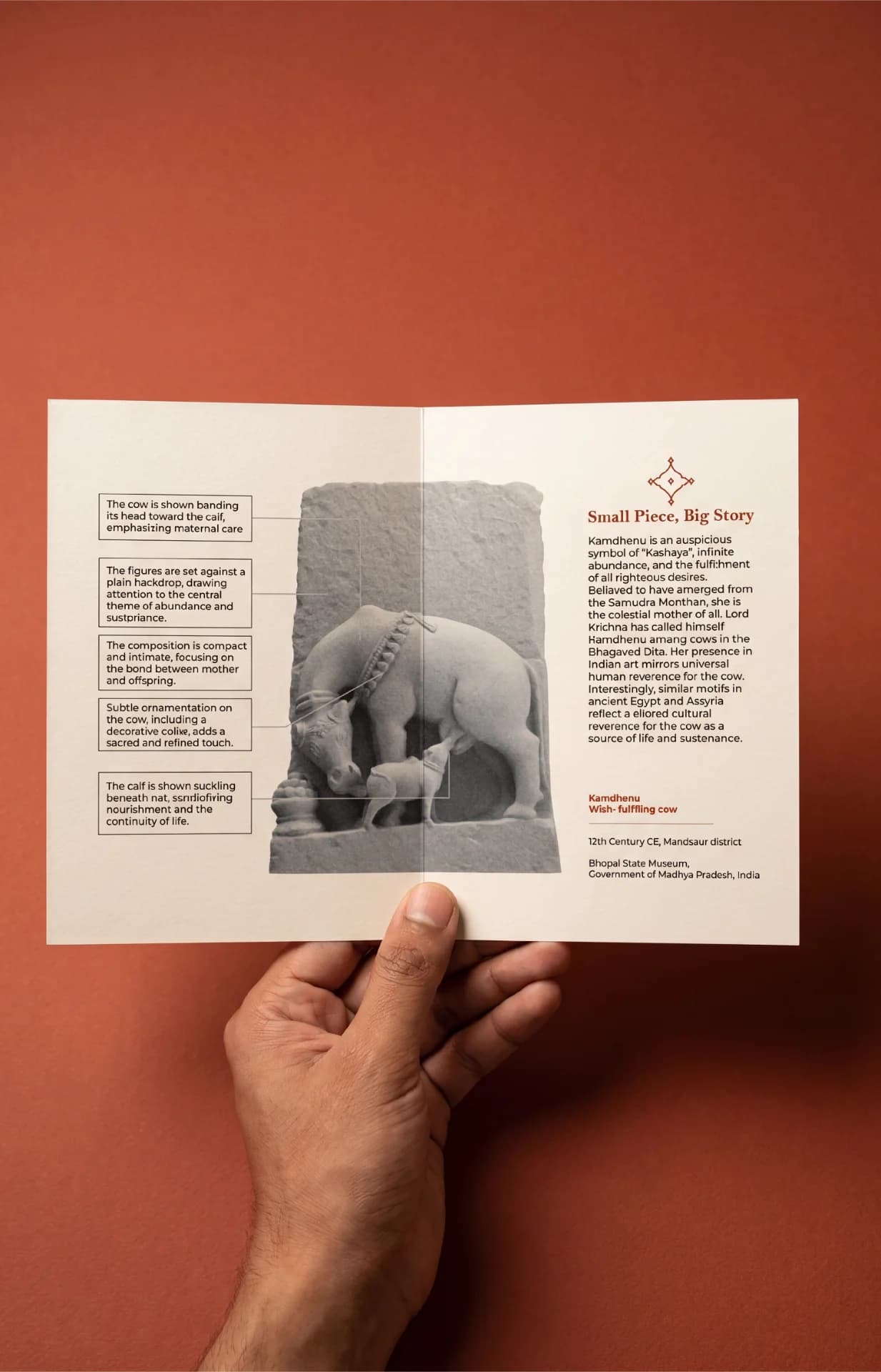A hand holds an informational brochure featuring the Kamdhenu Sculpture, showcasing detailed historical context and artistic analysis of the artifact.