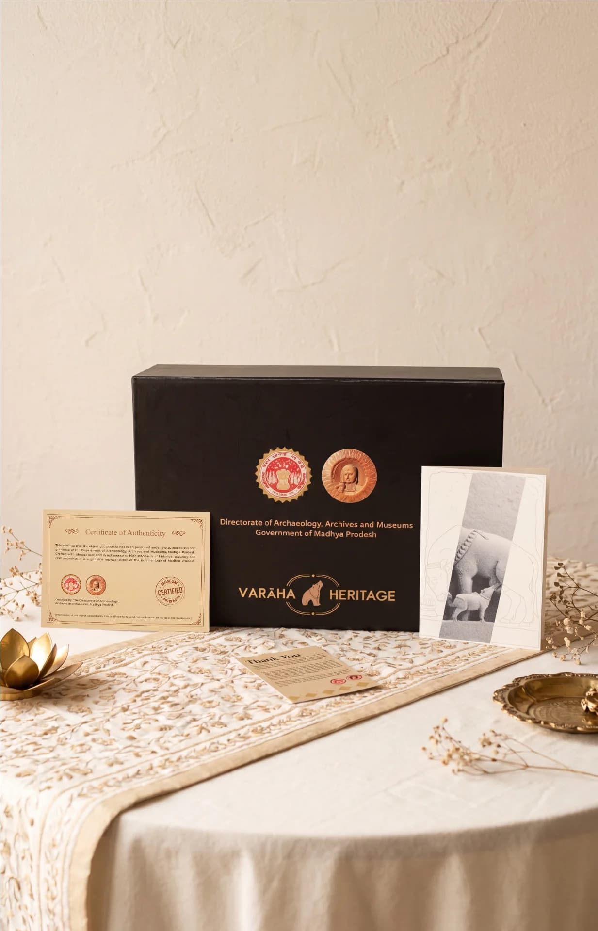 A black presentation box for the Kamdhenu Sculpture replica, featuring a certificate of authenticity and informational card on a table.