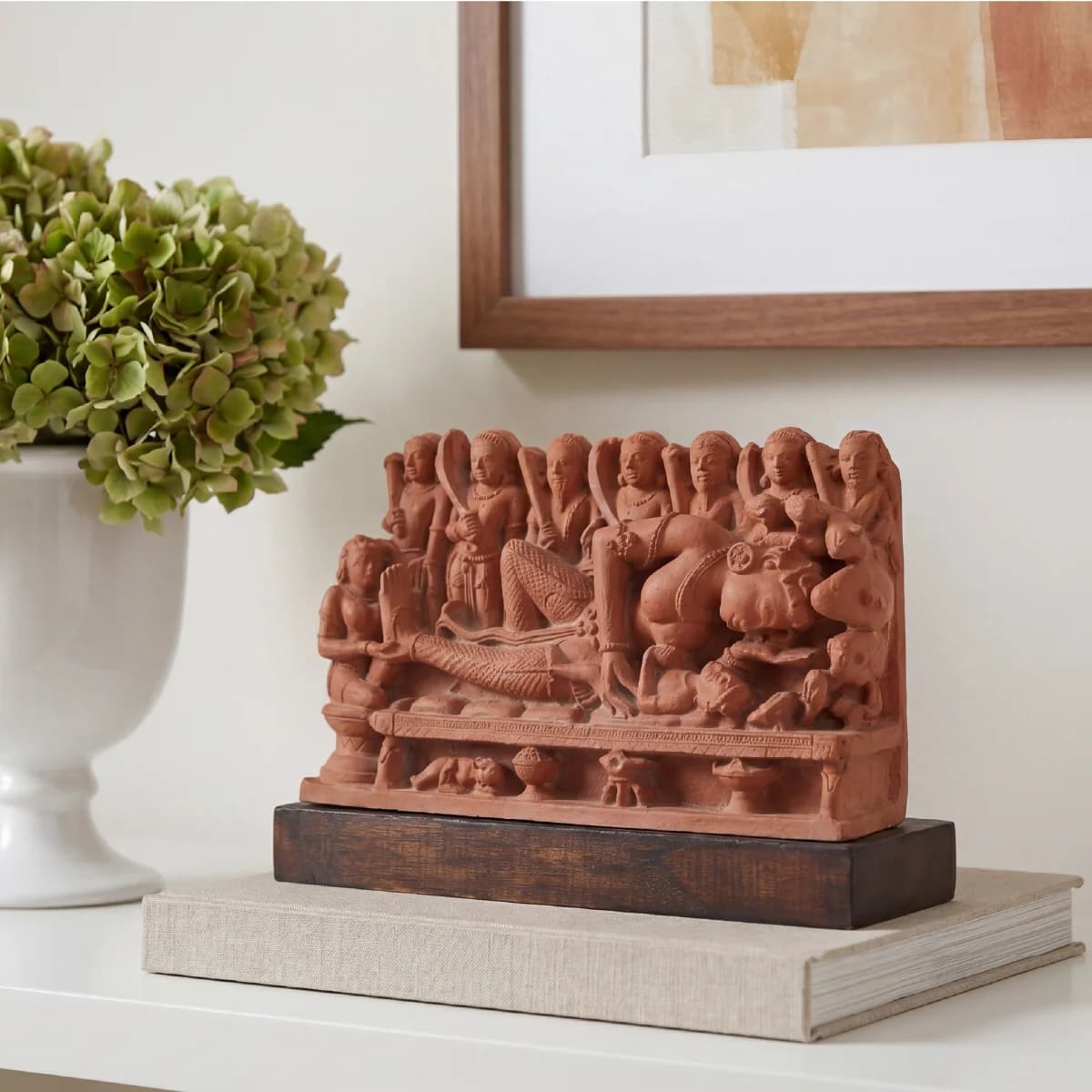 A terracotta Krishna's Birth Sculpture sits on a wooden base, displaying intricate 10th-century style carvings of Devaki and guards.
