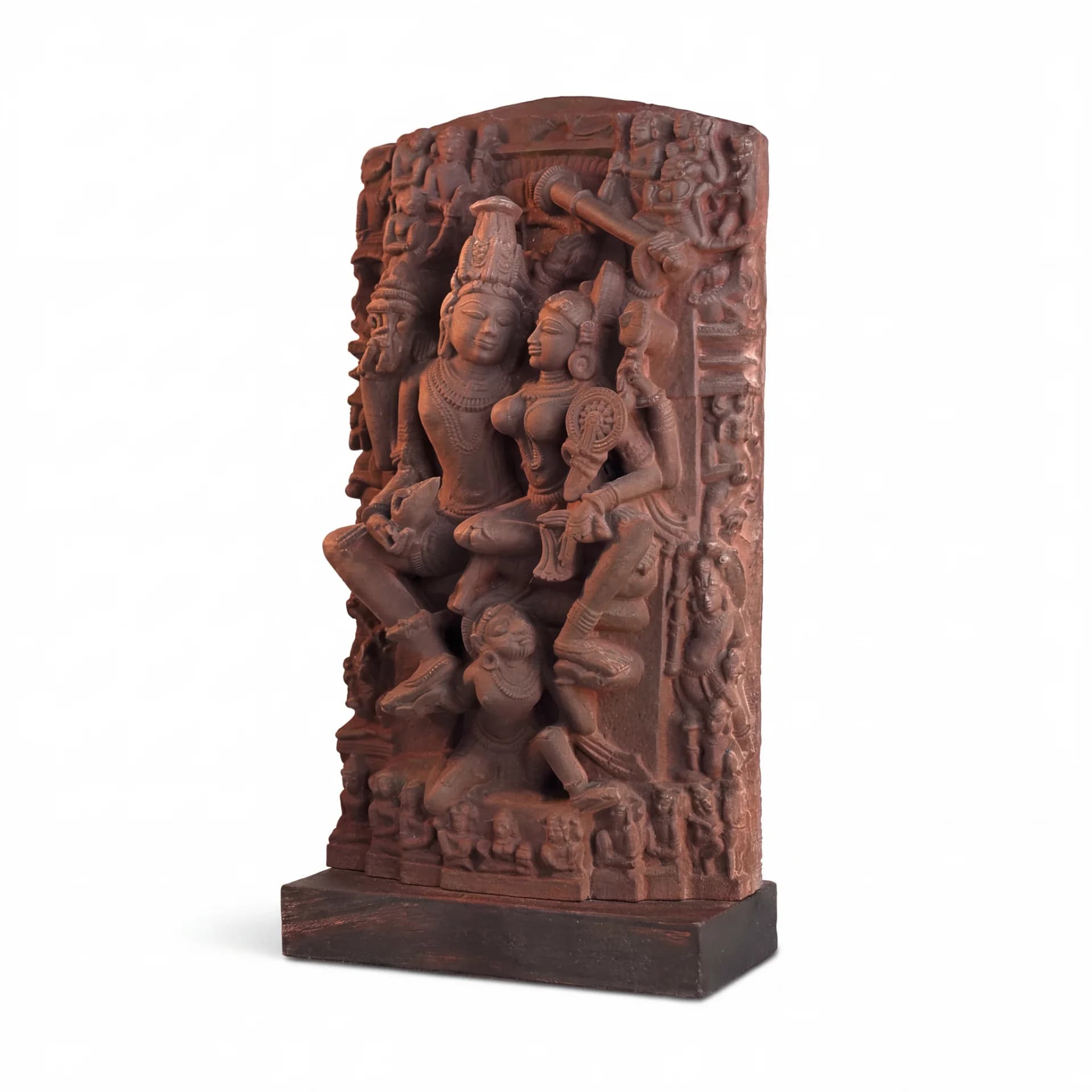 A detailed terracotta-style Lakshmi Narayan Sculpture displayed on stacked books next to a white vase with green flowers.