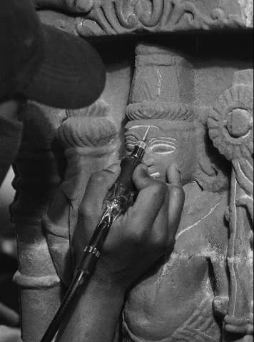 An artisan uses a precision tool to hand-carve the intricate sandstone features of a traditional deity replica statue.