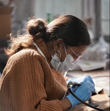 An artisan wearing protective gear carefully uses a rotary tool to refine a museum-replica artifact in a workshop.
