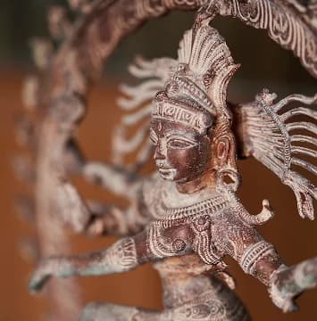 A close-up, three-quarter view of a bronze Shiva Nataraja statue, highlighting the intricate facial features and traditional headdress.