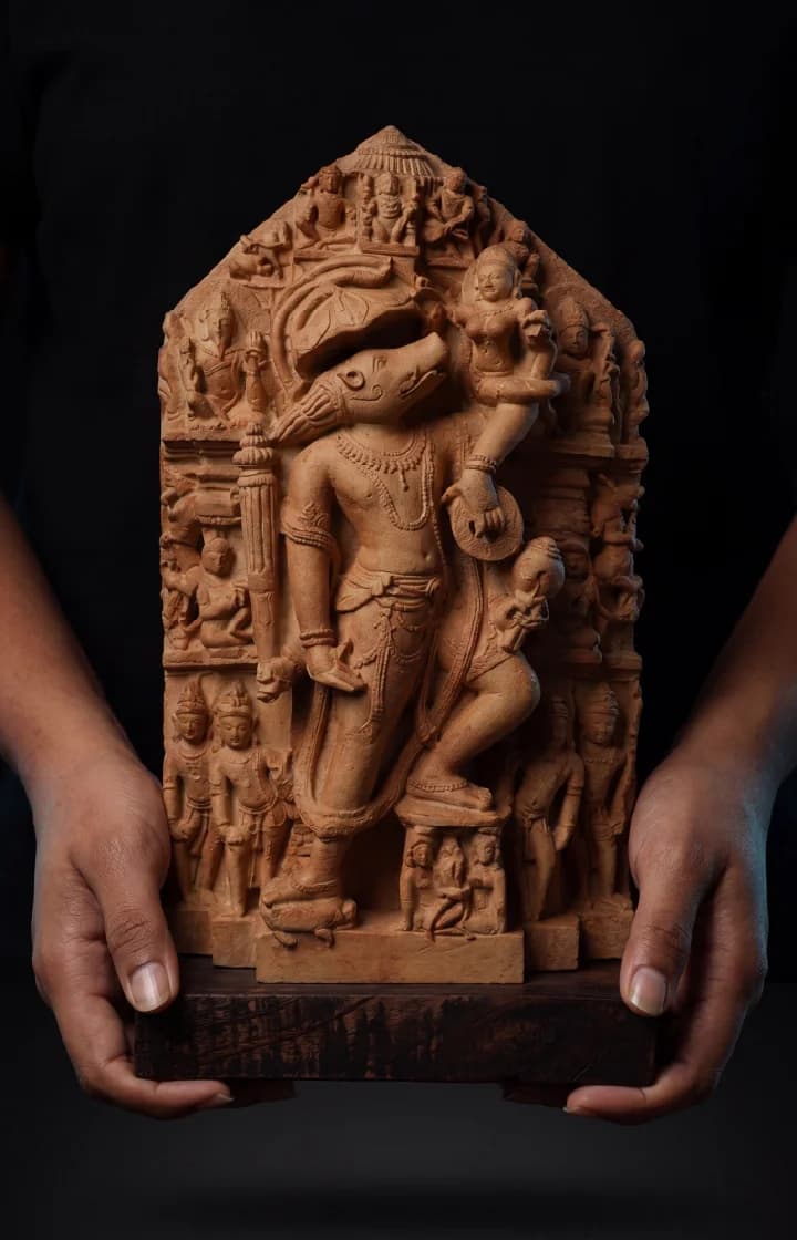 Hands hold a detailed stone composite Nar Varaha Sculpture, showing the man-boar deity carrying Bhudevi in a museum-replica style.