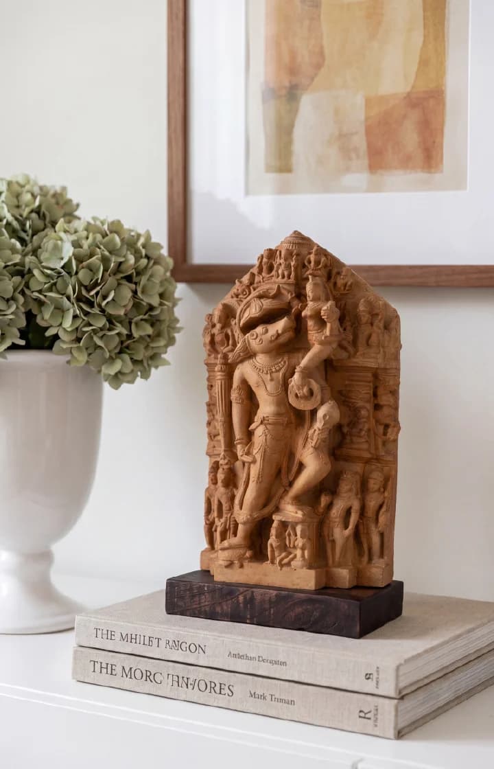 A Nar Varaha Sculpture replica in stone composite, displayed on books next to a vase of green hydrangeas.