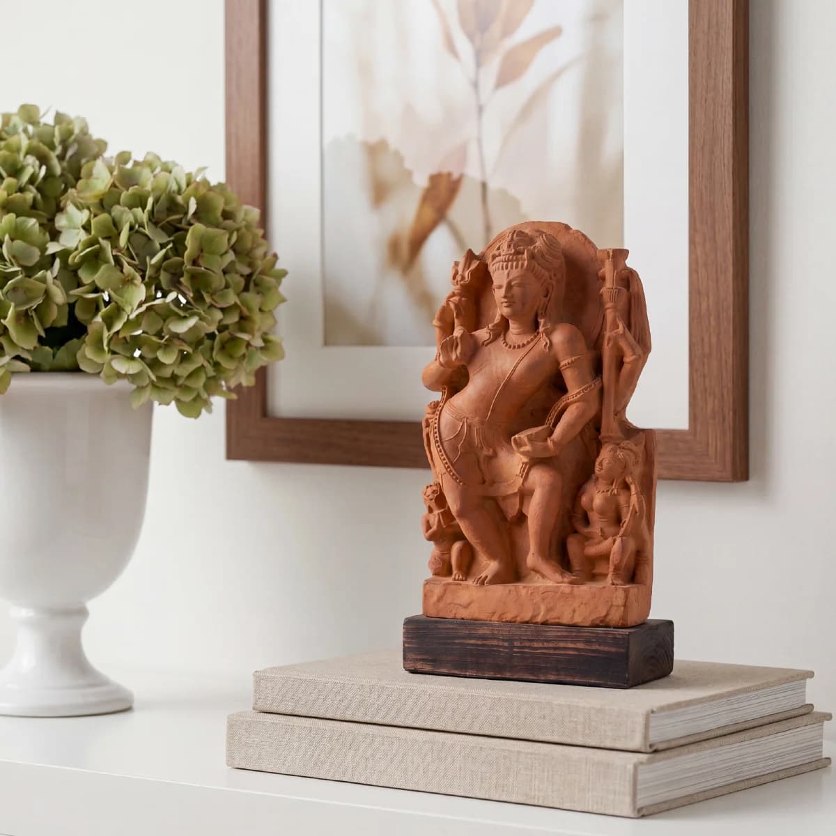 The Natesh Shiva Sculpture replica in stone composite displayed on stacked books next to a white vase.