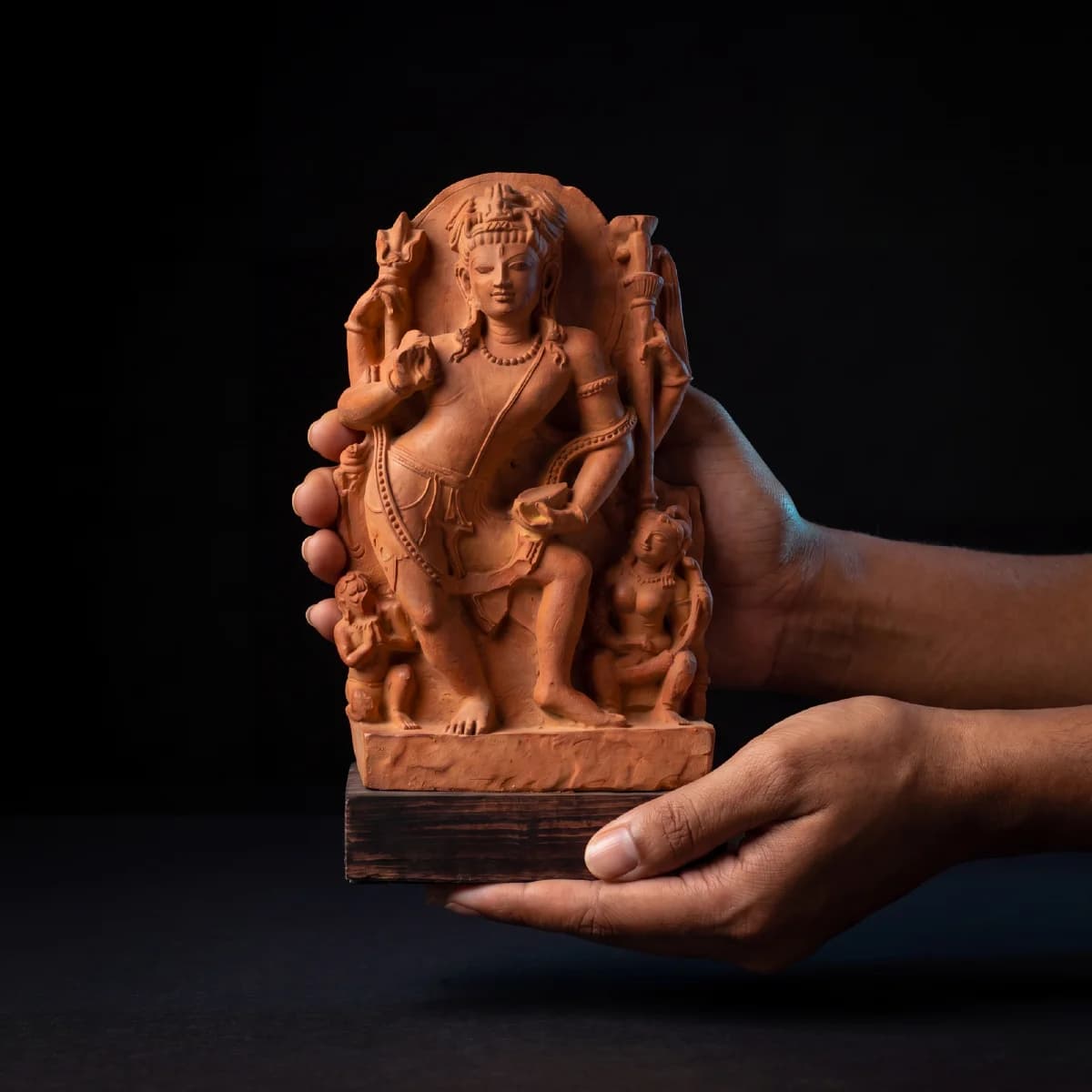 A pair of hands holds the Natesh Shiva Sculpture, a detailed stone composite replica featuring intricate Pratihara style carvings.