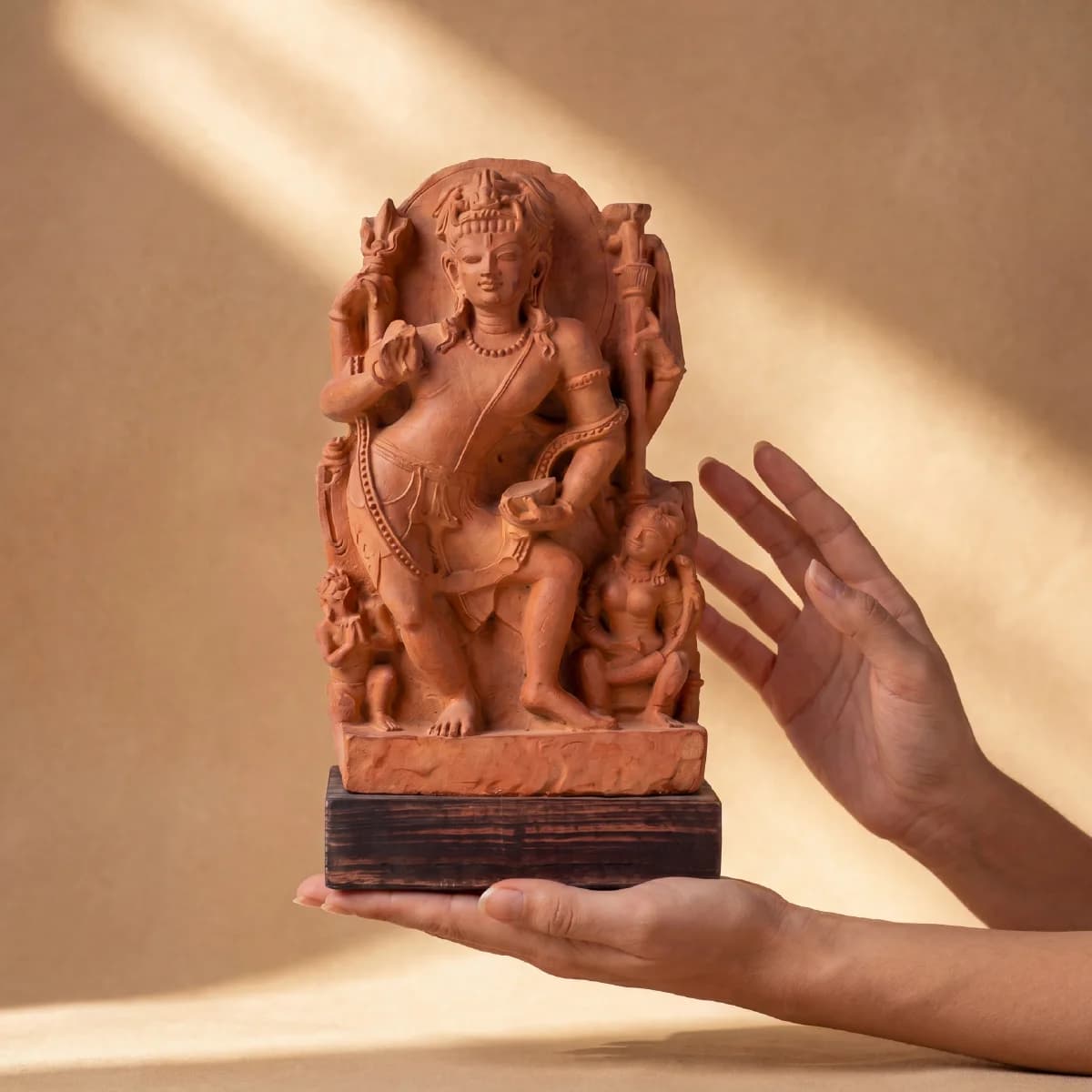 A pair of hands gently holds the Natesh Shiva Sculpture, a detailed stone composite replica of the dancing deity.