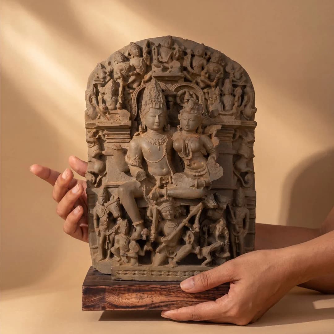 A pair of hands holds the Ravananugraha Sculpture, a detailed stone composite replica featuring Shiva and Parvati against a dark background.
