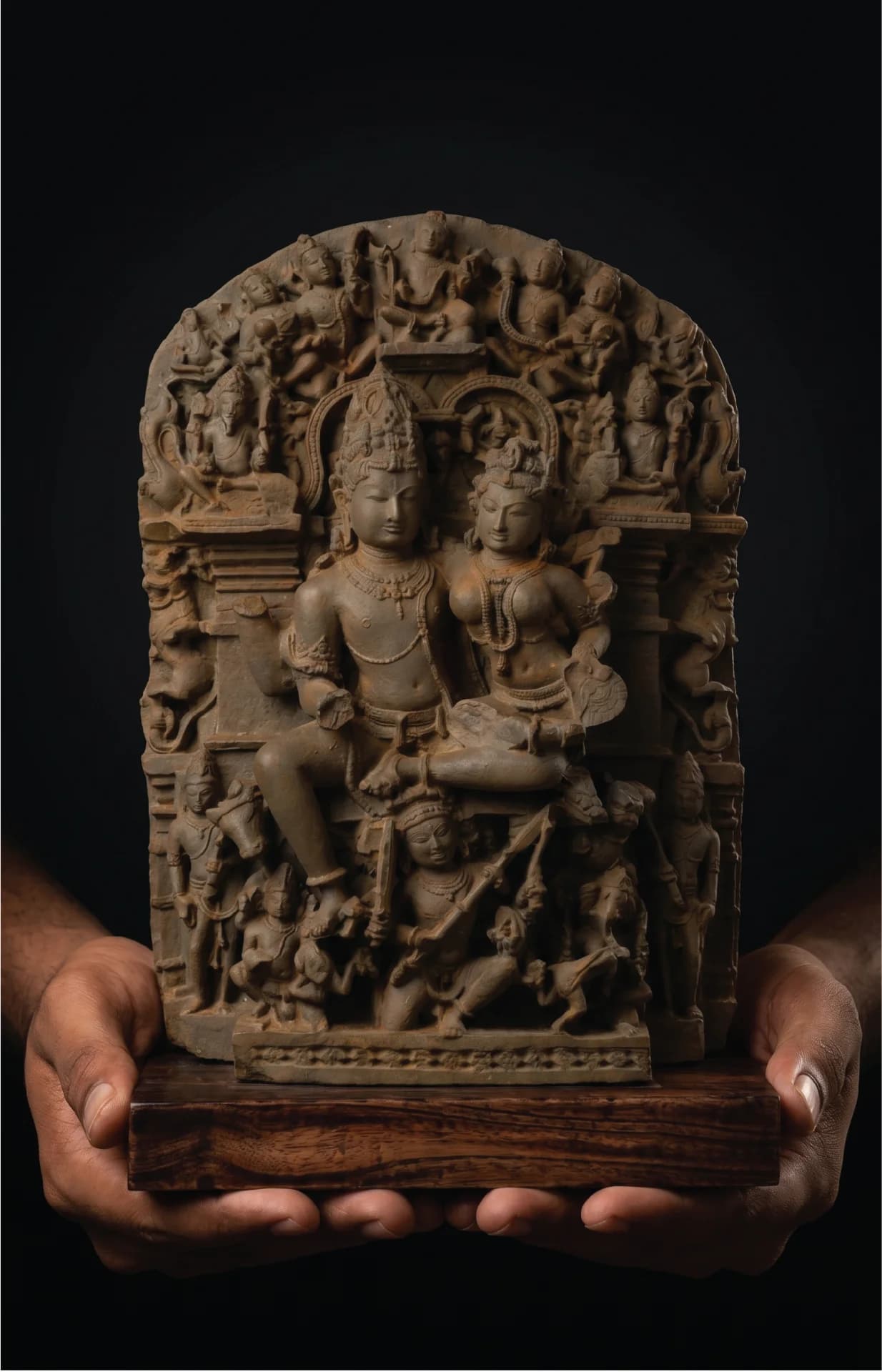 Hands hold a stone composite Ravananugraha Sculpture replica featuring intricate 11th-century style carvings of Shiva and Parvati on a teak base.