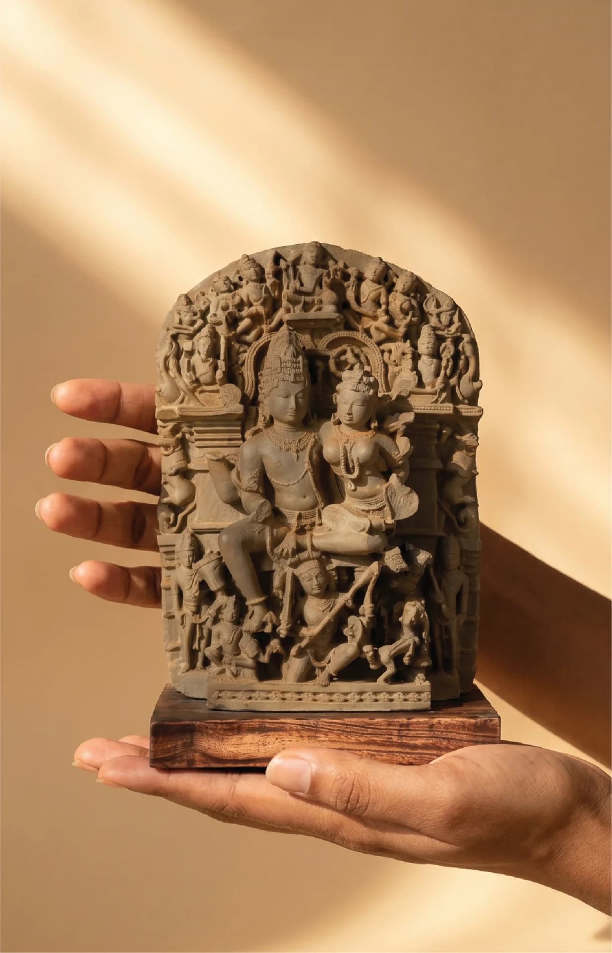 A person holds a stone composite Ravananugraha Sculpture replica, showcasing intricate 11th-century temple art details mounted on teak wood.