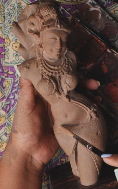 An artisan uses a precision tool to hand-carve the intricate sandstone features of a traditional deity replica statue.