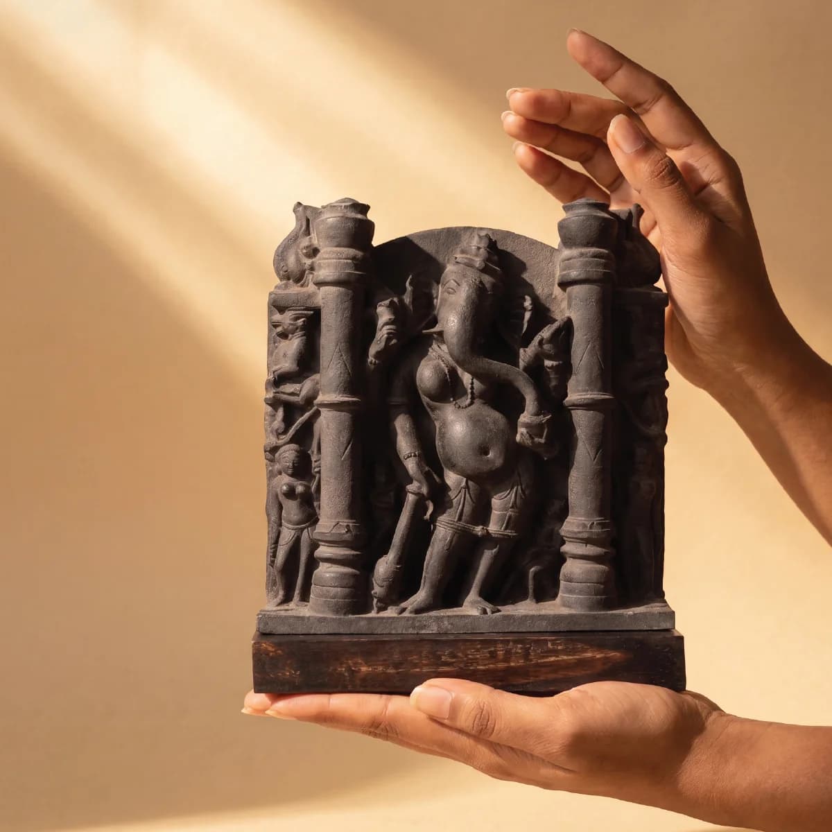 A pair of hands carefully cradles a dark stone Vinayaki Sculpture, showcasing the intricate temple art replica details.