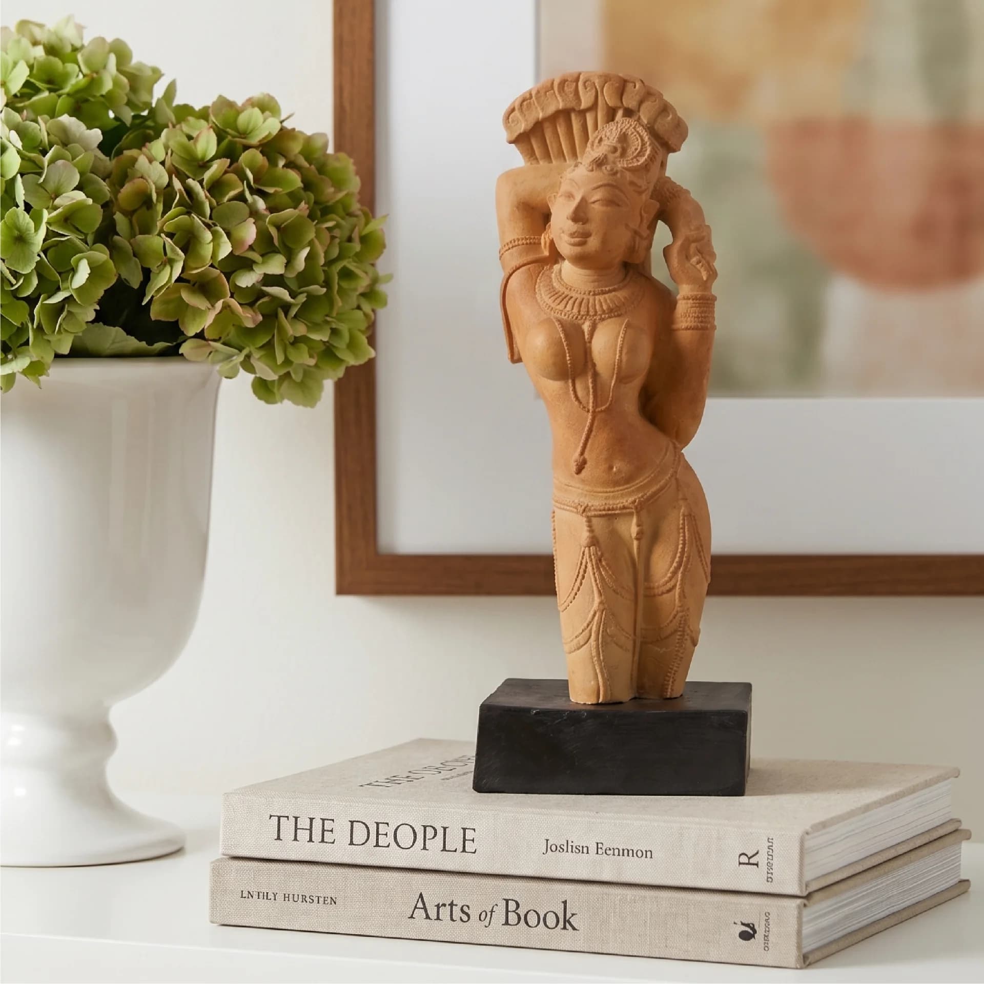 The Alasa Nayika Sculpture stands on a black base atop stacked books, showcasing intricate terracotta-style craftsmanship and elegant temple art details.