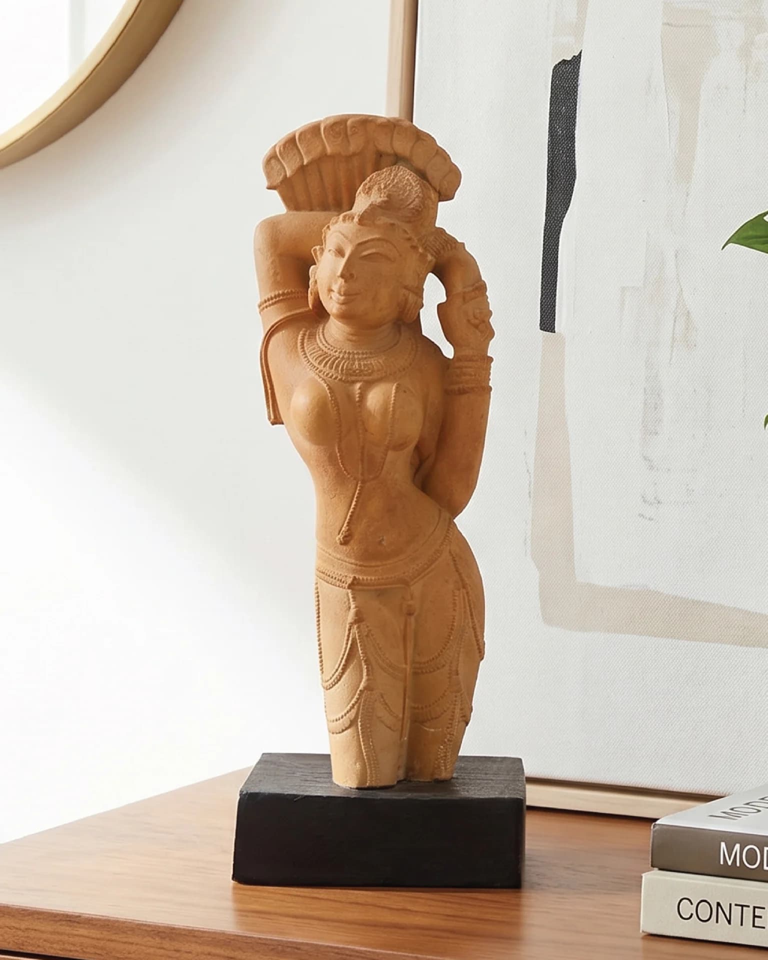 A sandstone-finish Alasa Nayika Sculpture standing on a dark wooden base, captured in a bright, modern interior setting.