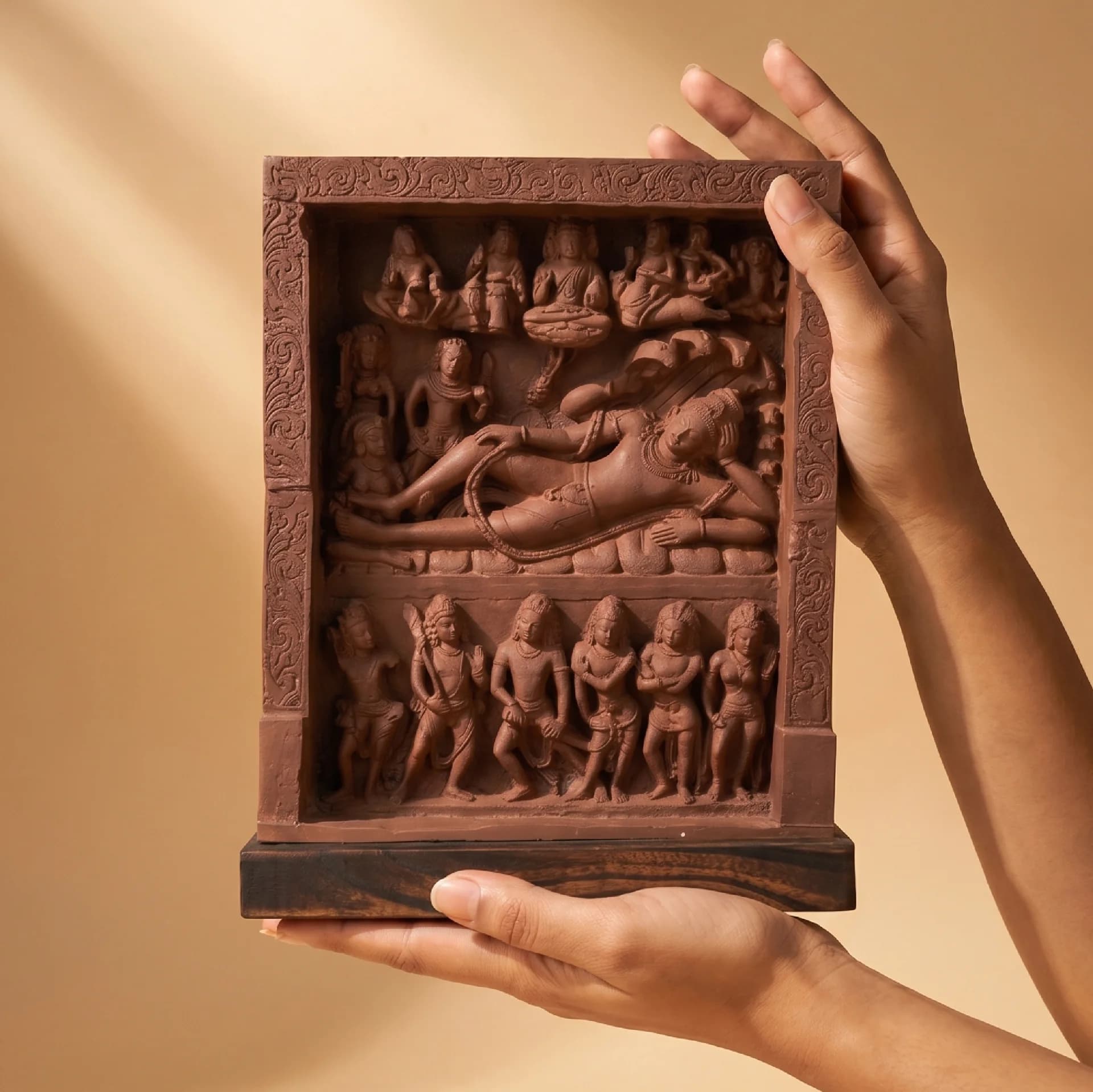 A pair of hands holds a terracotta-style Anantasayana Vishnu Sculpture, showcasing the intricate relief detail of the reclining deity.
