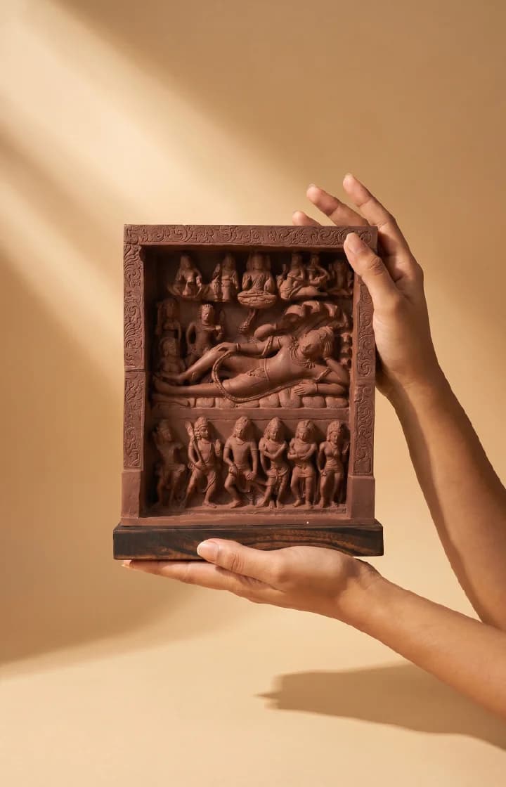 A pair of hands holds an Anantasayana Vishnu Sculpture, a terracotta-style relief panel depicting a reclining deity on a serpent.
