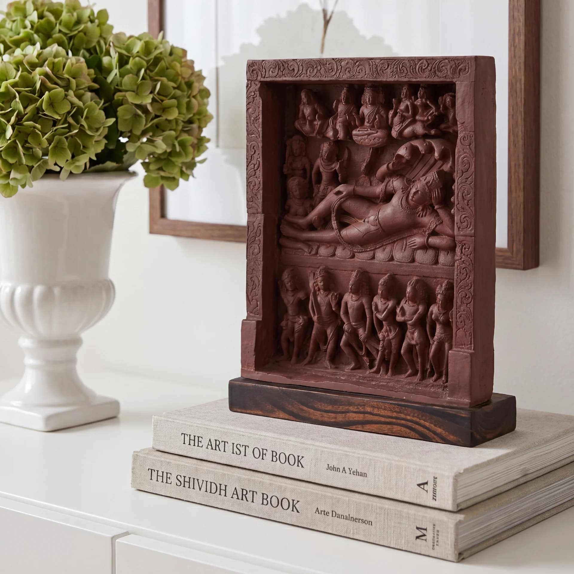 An Anantasayana Vishnu Sculpture replica in terracotta finish displayed on stacked books next to a white vase.