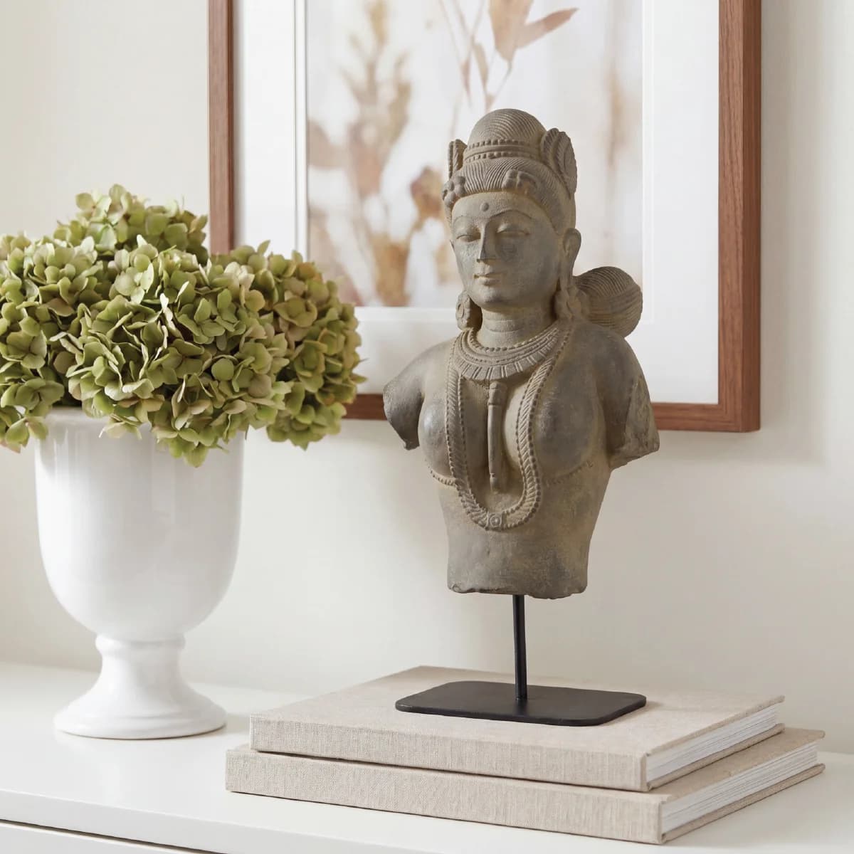 A Female Figure Bust Sculpture in stone composite displayed on a stack of books next to a white vase.