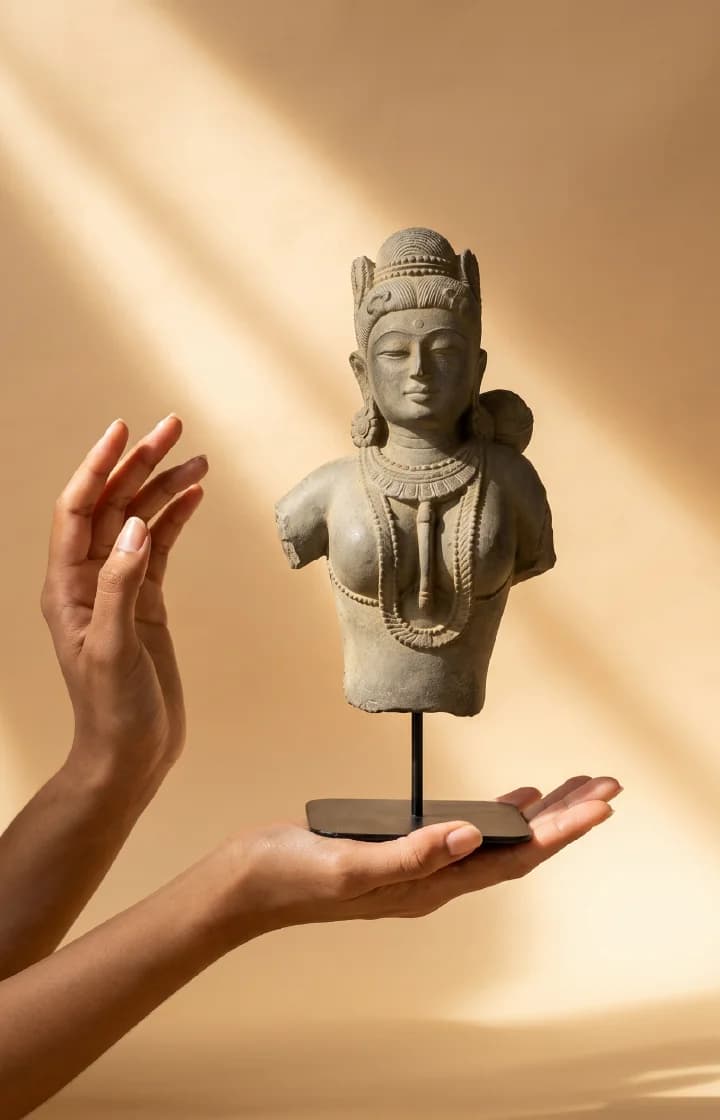 A pair of hands gently cradles a Female Figure Bust Sculpture, showcasing the detailed Chola style stone composite craftsmanship.