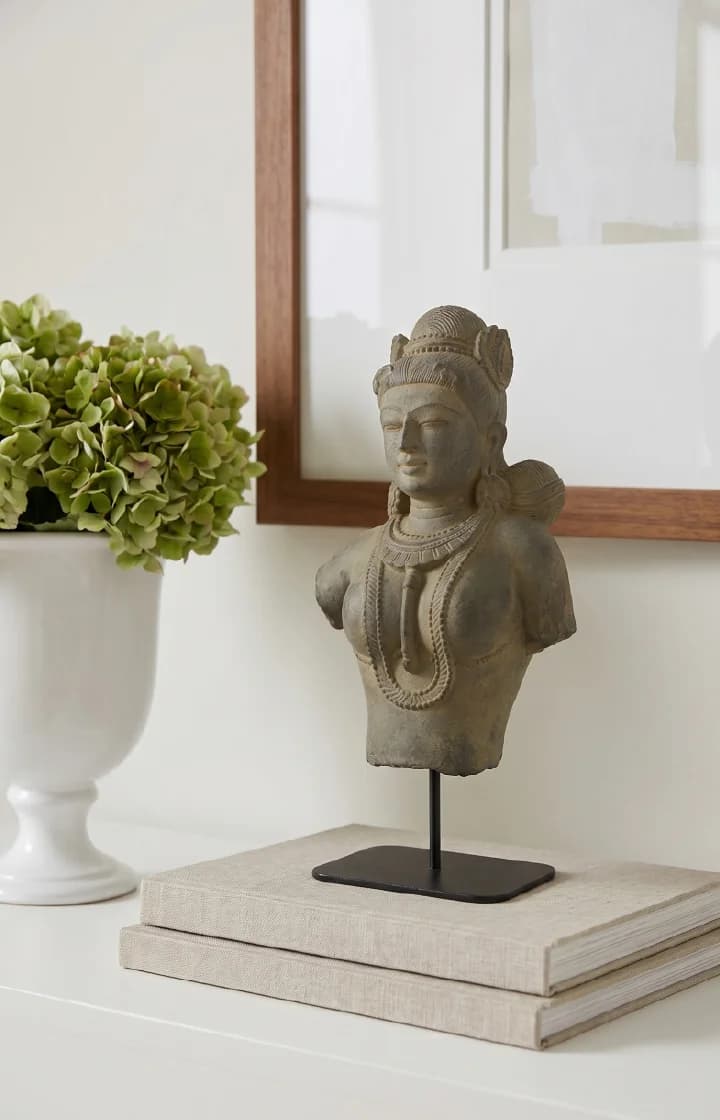 A Female Figure Bust Sculpture in stone composite displayed on a stand atop stacked books in a home setting.