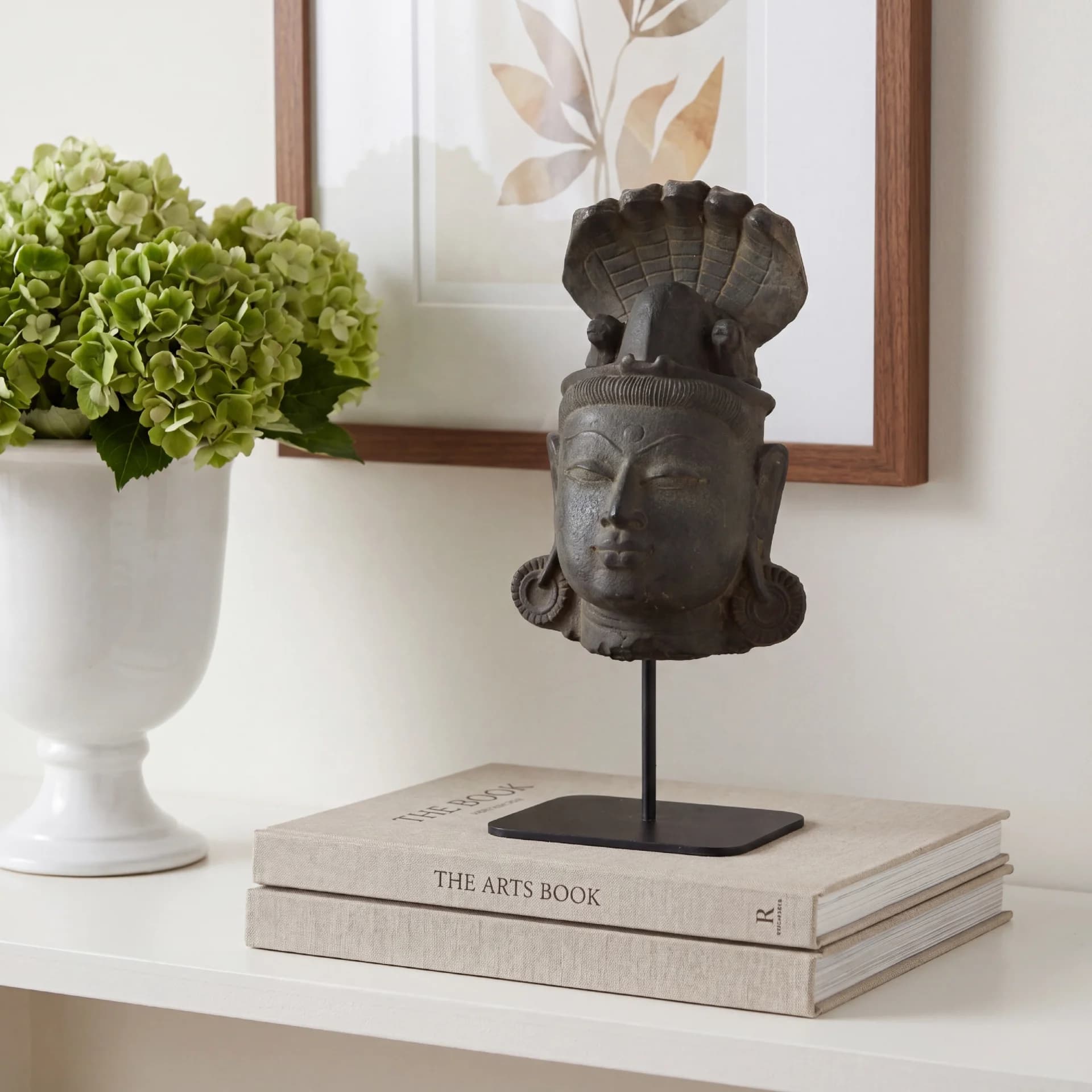 A stone composite Shiva Lingam with Nandi & Serpent replica displayed on a metal stand atop decorative books.
