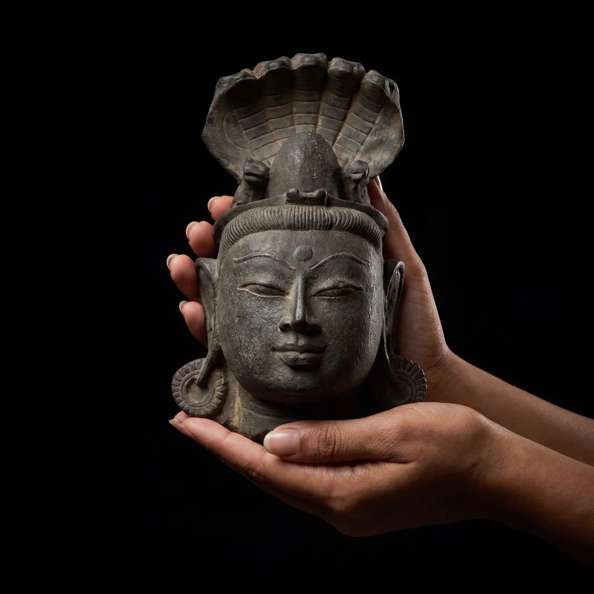 Hands cradling a Shiva Lingam with Nandi & Serpent stone composite replica, showcasing the serene facial features and intricate carving.