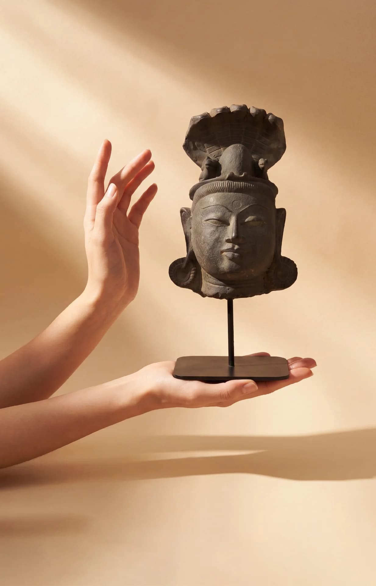 A pair of hands gently cradles the Shiva Lingam with Nandi & Serpent stone composite replica against a neutral background.