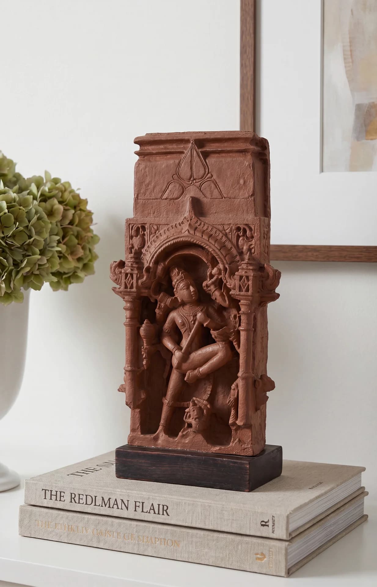 A Gajasura Vadha Sculpture replica in stone composite, displayed on a stack of books, showing intricate temple relief carvings.