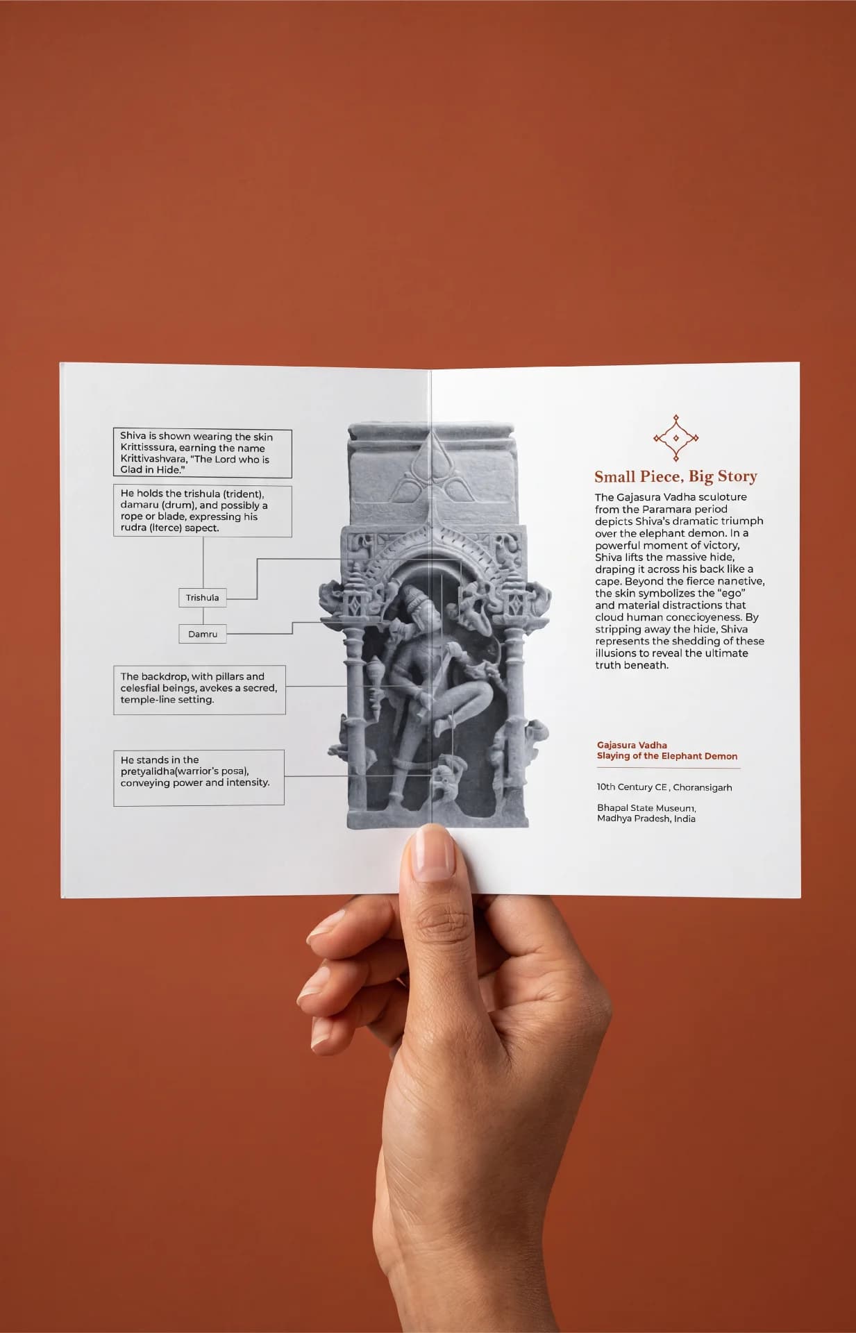 A hand holds an informational brochure featuring the Gajasura Vadha Sculpture, displaying detailed stone composite relief diagrams and historical context.