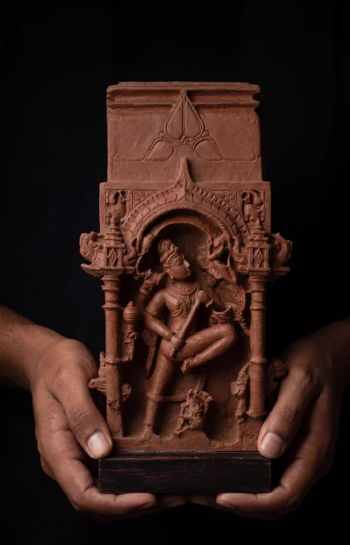 Hands holding a stone composite Gajasura Vadha Sculpture, showcasing the intricate 10th-century temple relief detail against a dark background.