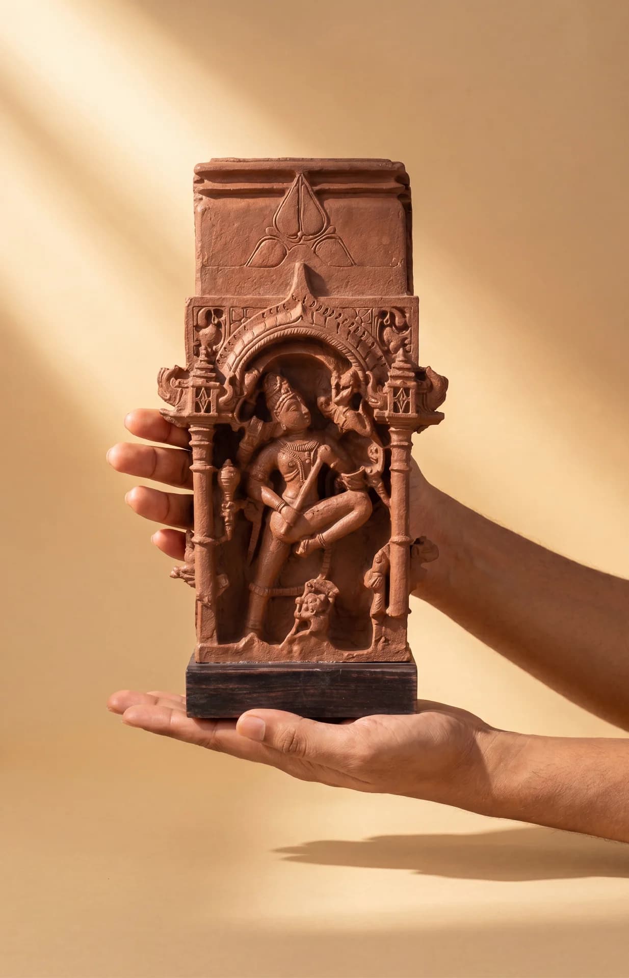A pair of hands holds the Gajasura Vadha Sculpture, a stone composite replica featuring intricate 10th-century temple relief carvings.