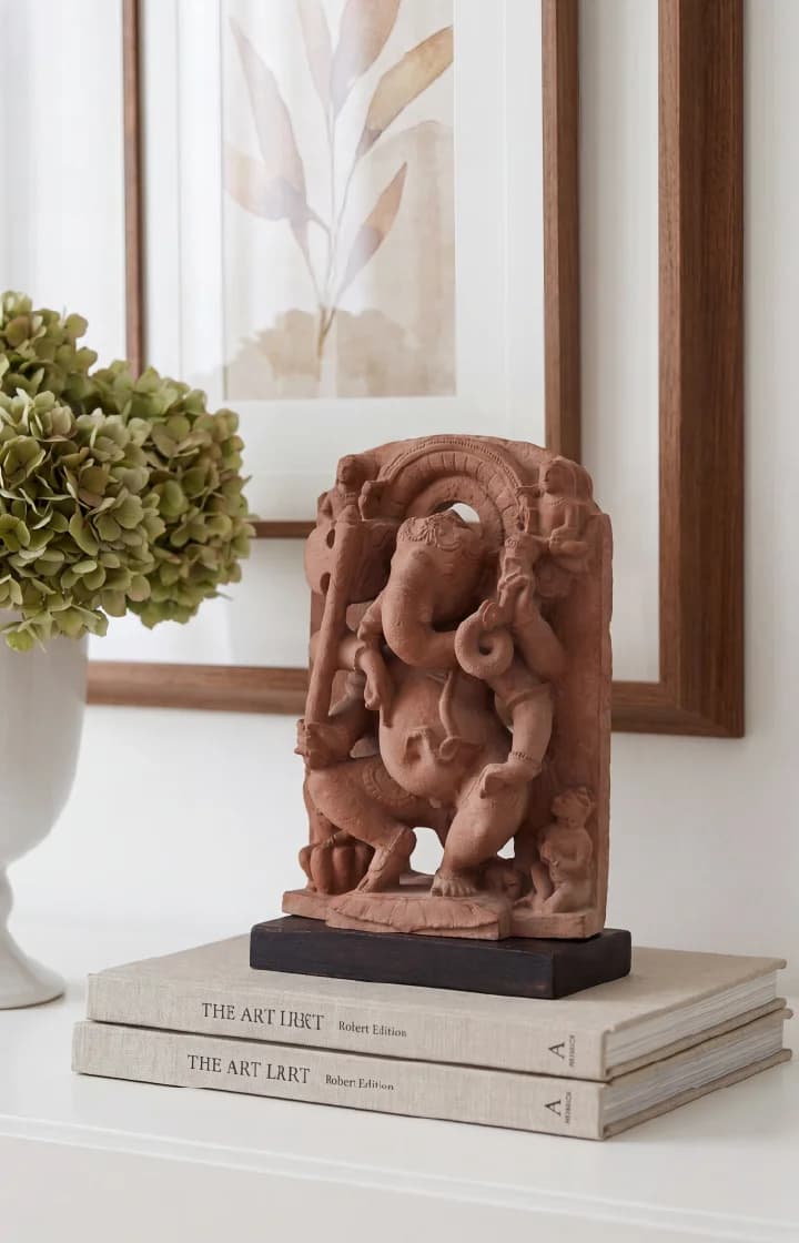 A Ganesha Sculpture Hindu Elephant God Temple Art Replica, handcrafted in terracotta, displayed on stacked books in a home setting.