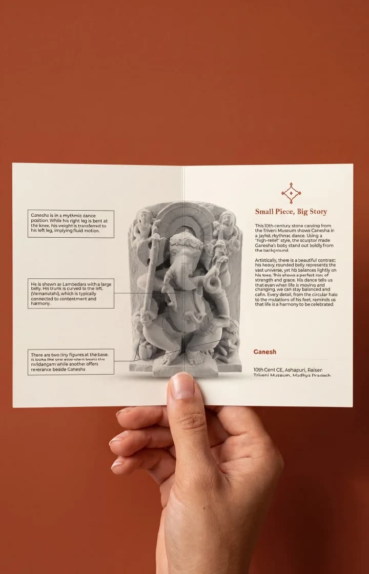 A hand holds an informational brochure featuring the Ganesha Sculpture, displaying detailed stone carving analysis and historical context.