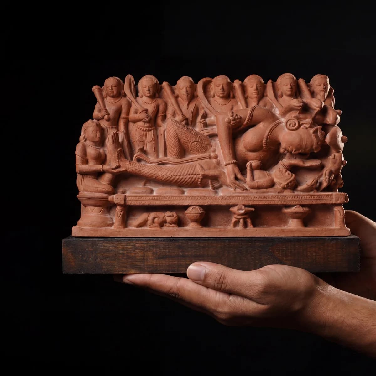 A person holds a detailed Krishna's Birth Sculpture, a handcrafted terracotta replica featuring intricate figures from 10th-century temple art.